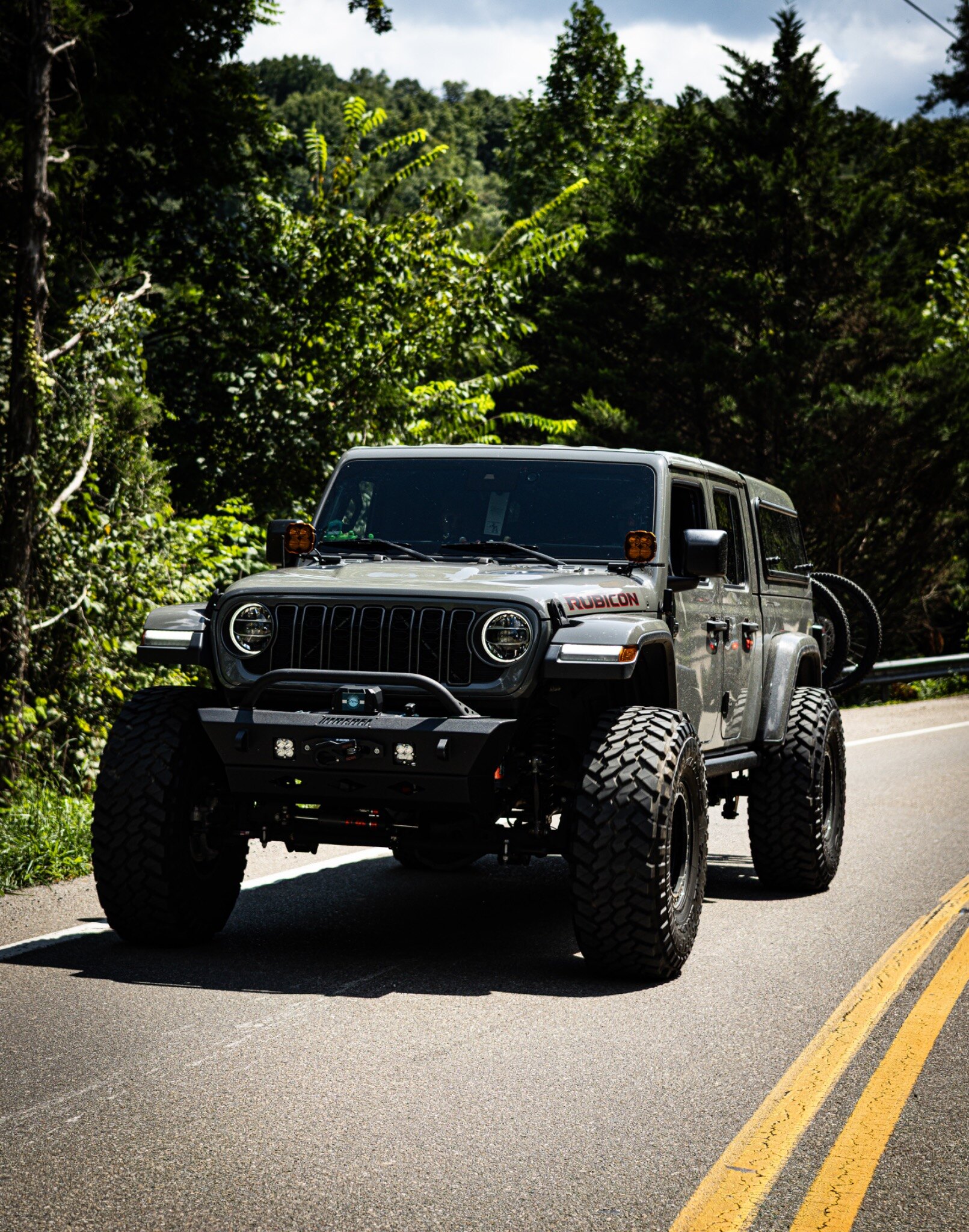 A lifted silver Jeep Wrangler Rubicon driving through a wooded curve
