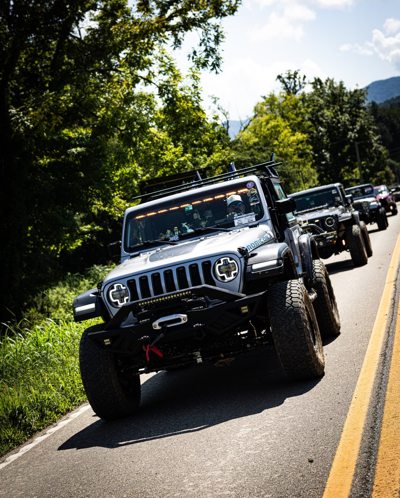 A silver Jeep Wrangler leading a line of Jeeps along a mountain road